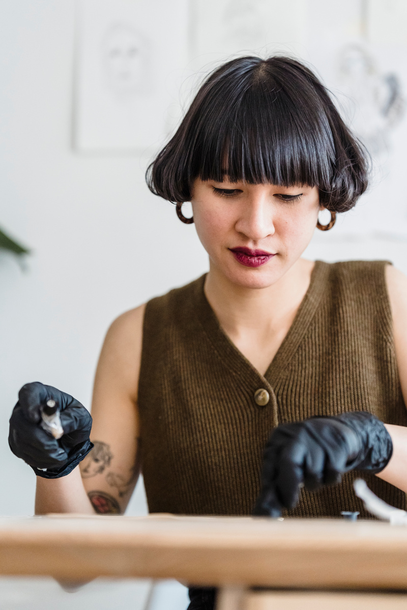 Focused Asian female designer using tattoo machine during practice